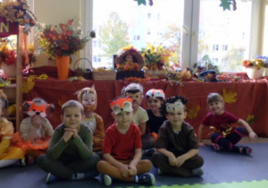 Grupka dzieci siedząca na tle kącika jesieni.